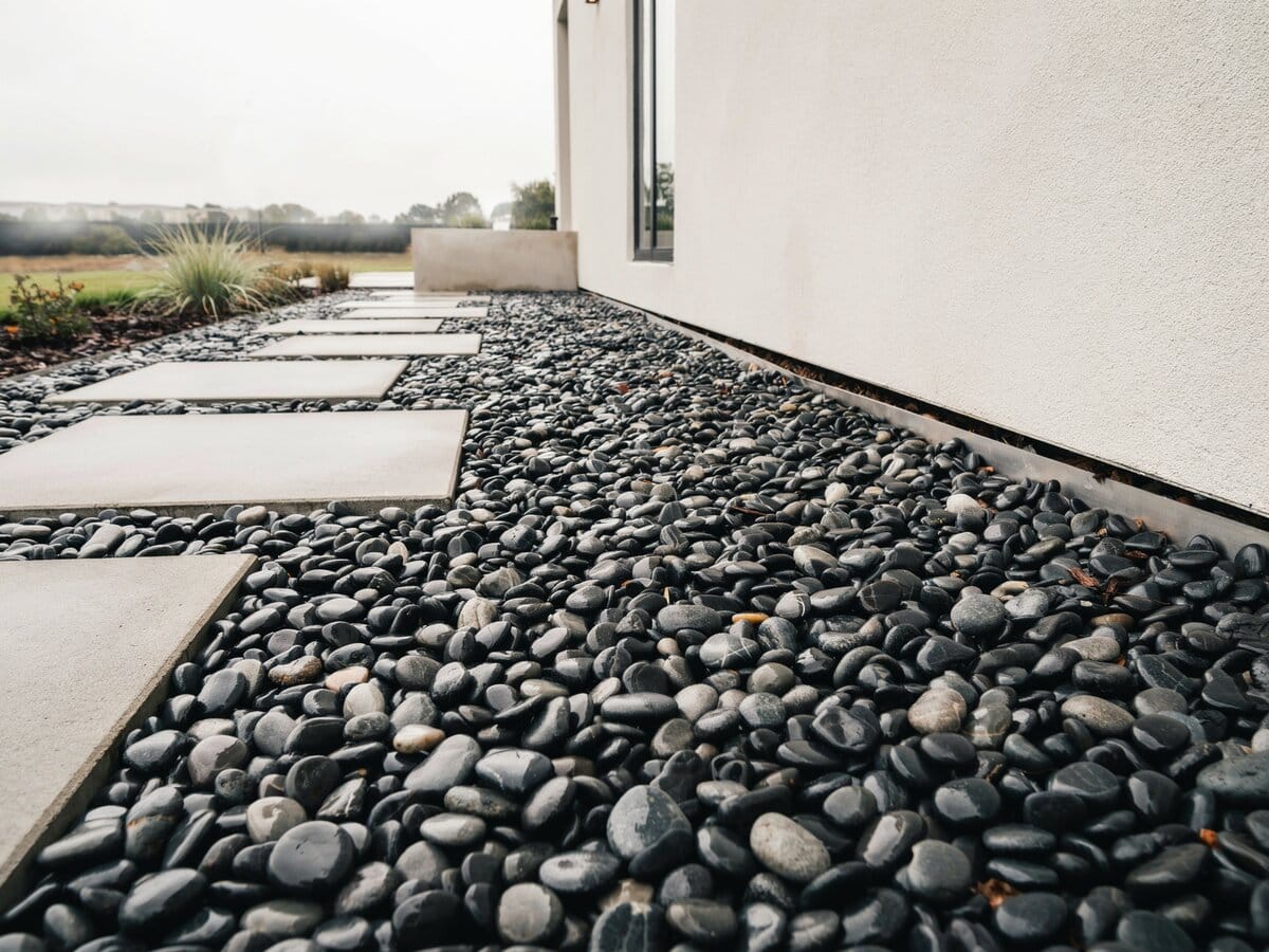 Modern square concrete pavers on black polished river pebbles along a side yard of a contemporary home