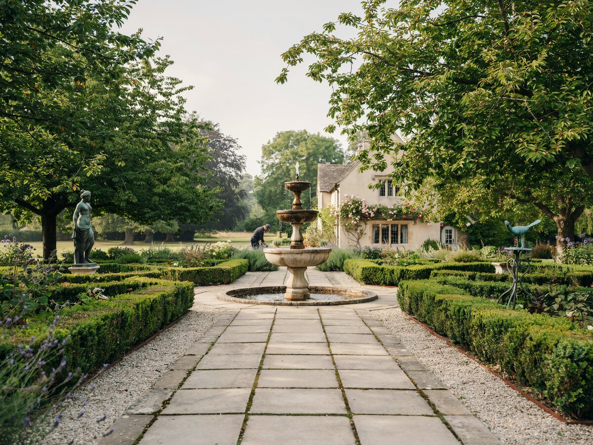 Square concrete pavers through a formal garden with a tiered fountain boxwood hedges and bronze sculptures
