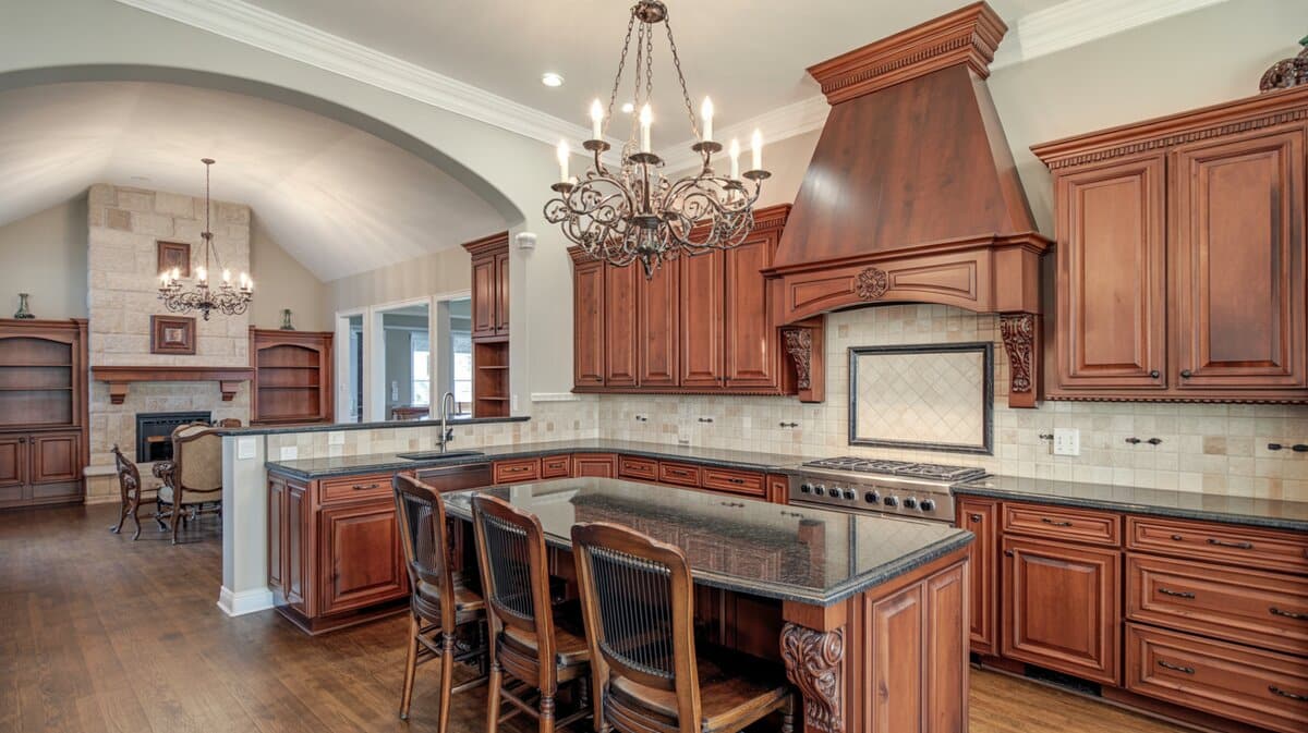 Rich cherry wood kitchen with matching carved range hood, wrought iron chandelier, and stone alcove backdrop