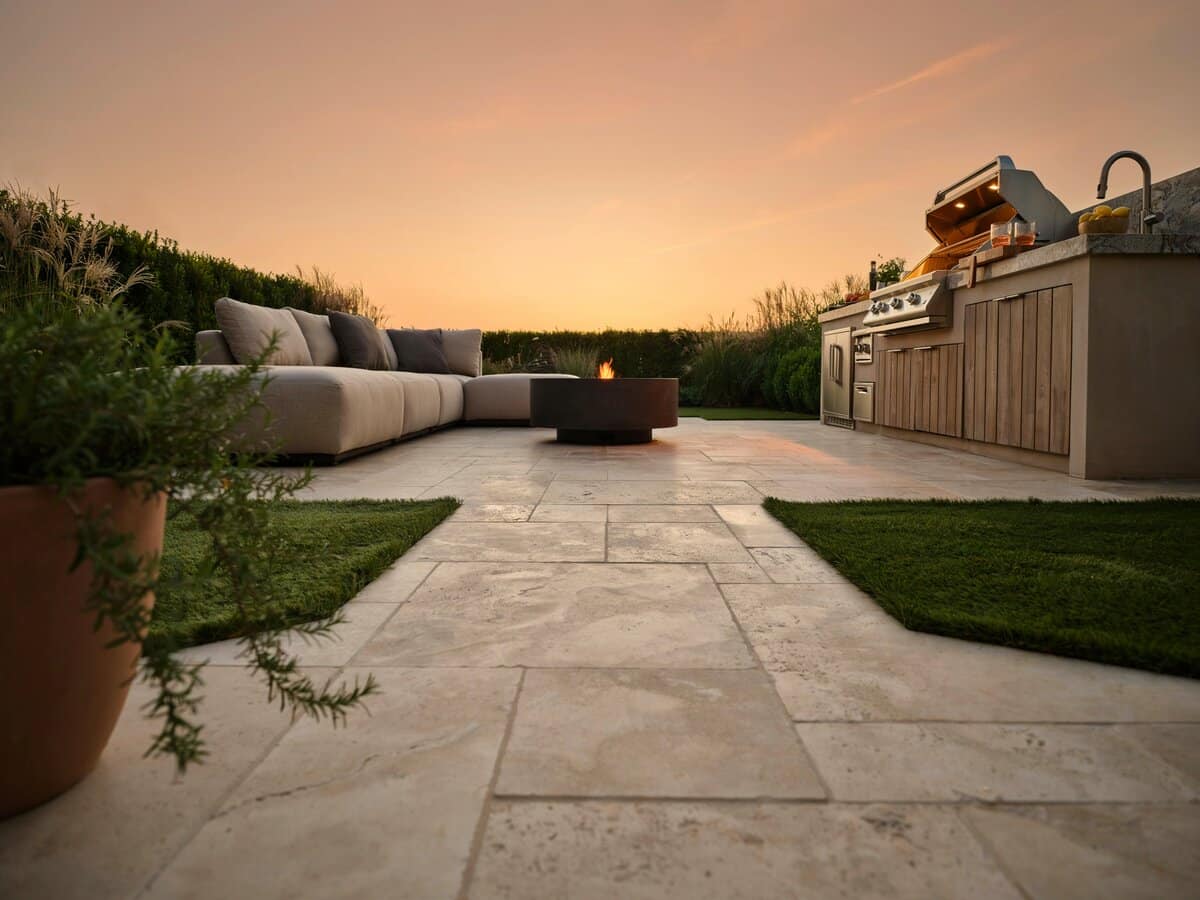 Travertine paver walkway and patio with artificial turf next to an outdoor kitchen at sunset