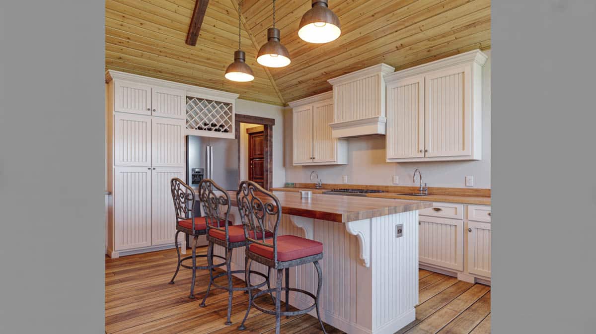 Beadboard kitchen cabinets in white with a butcher block island and red-cushioned iron barstools