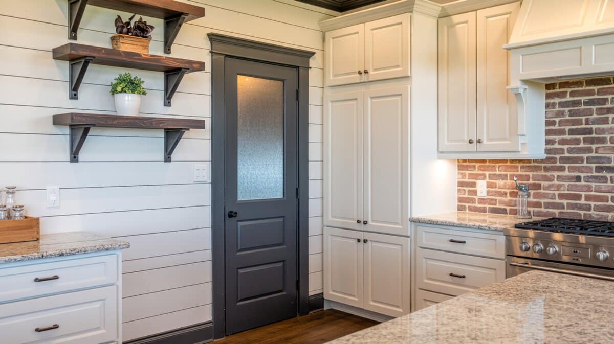 White farmhouse kitchen with charcoal painted pantry door against shiplap accent wall and brick backsplash