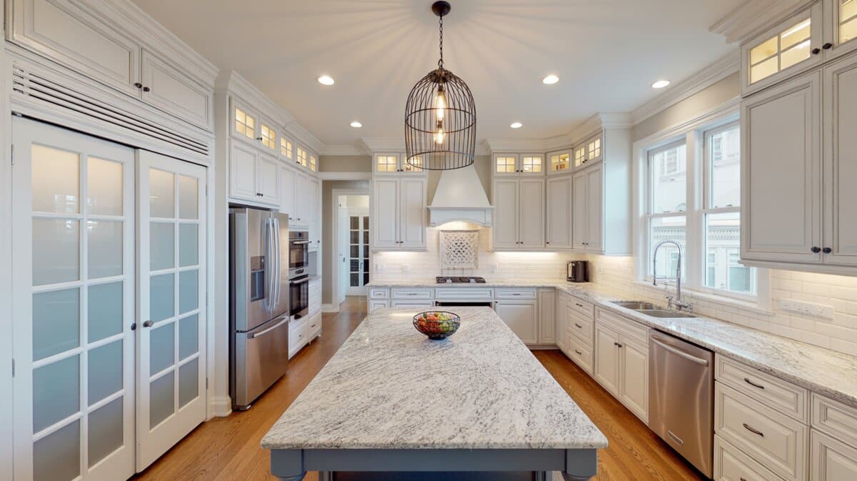 Modern white kitchen with frosted glass pantry door and large swirled gray and white granite island