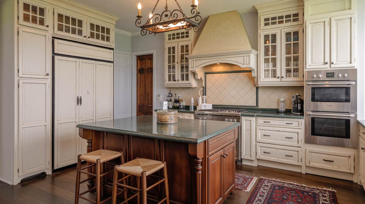 Antique white raised-panel cabinets with a cherry island and ornate wrought-iron chandelier above