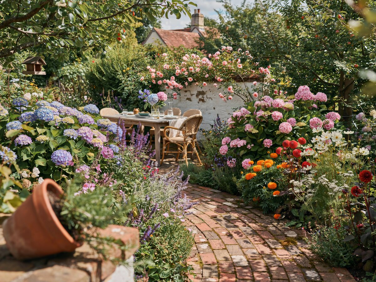 Winding brick paver path through a colorful cottage garden with hydrangeas leading to patio dining
