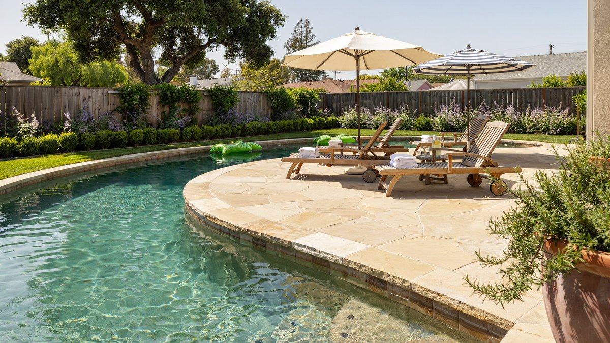 Backyard lazy river pool wrapping a stone patio with lounge chairs