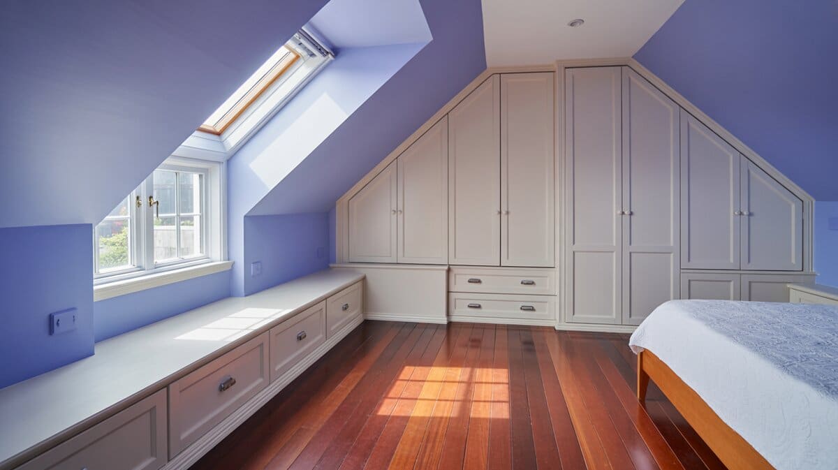 Attic bedroom with blue walls, white storage bench and skylight window