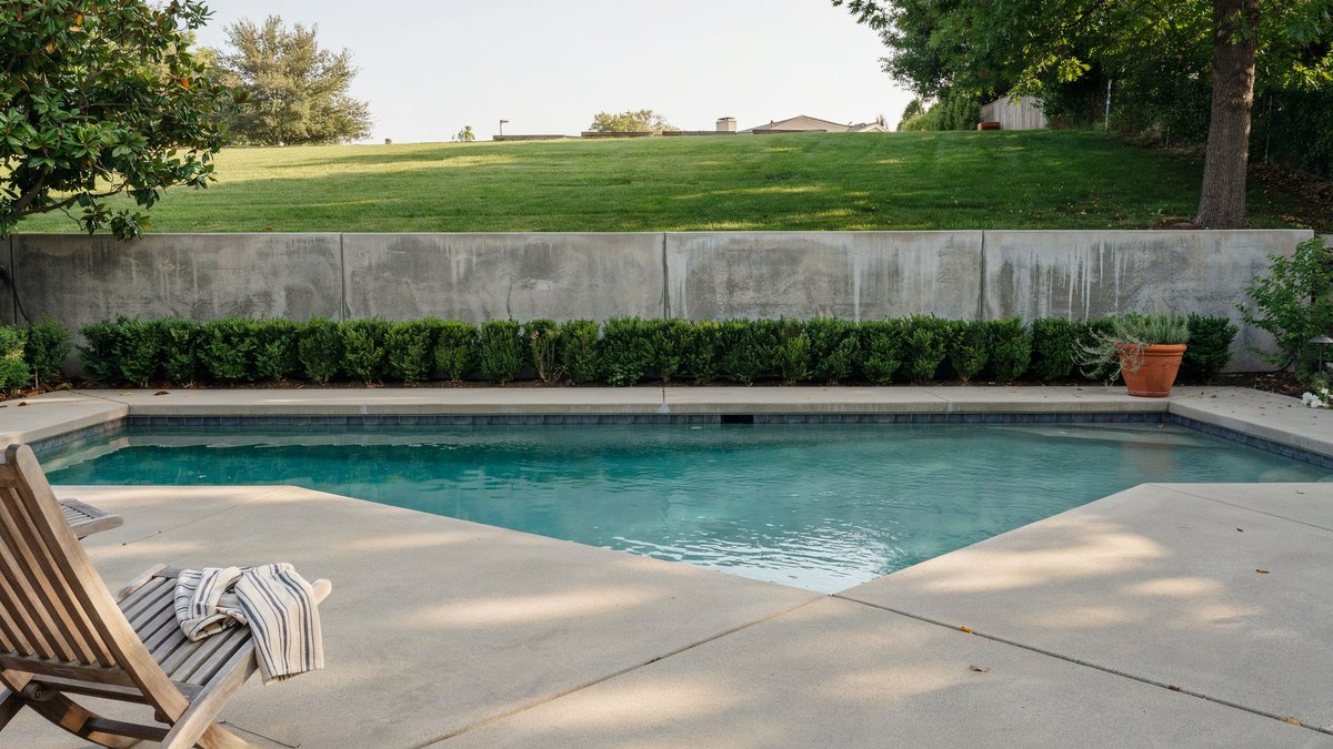 Poured concrete wall with boxwood row holding back a green lawn above a pool