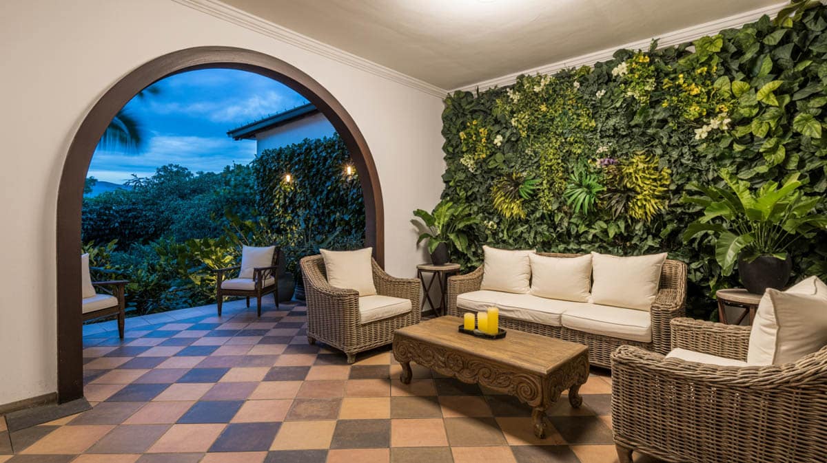 Elegant covered patio at dusk with arched opening, terracotta tile floor, wicker furniture, and living green wall