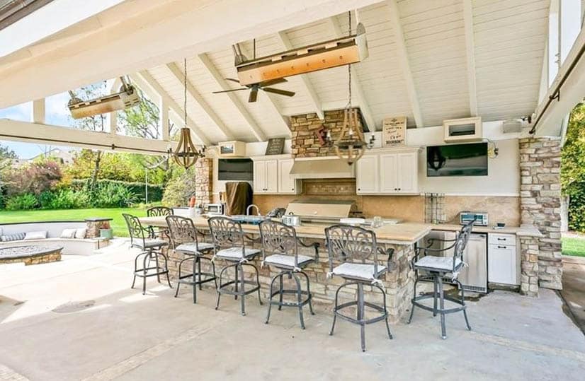 Covered outdoor kitchen with concrete countertop bar and white cabinets