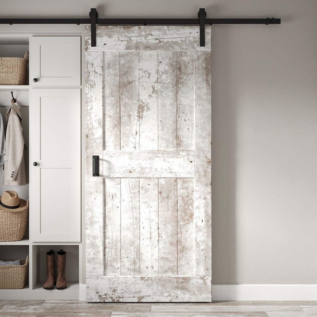 Distressed white-painted barn door with matte black hardware next to built-in white mudroom storage cabinets