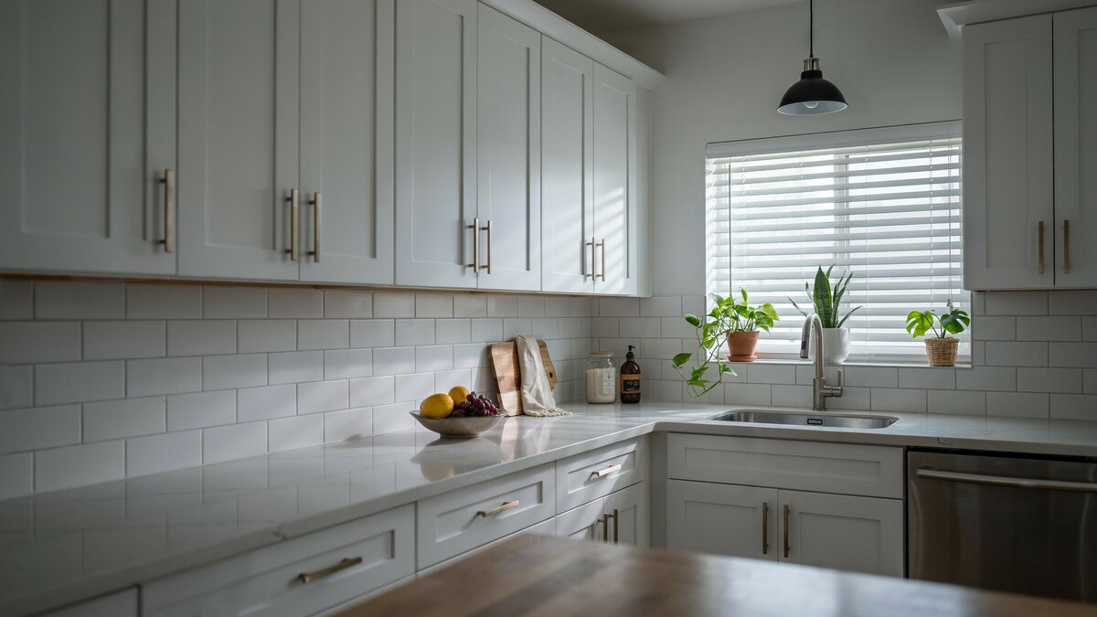 Corner window with blinds and plants beside white cabinets and countertops