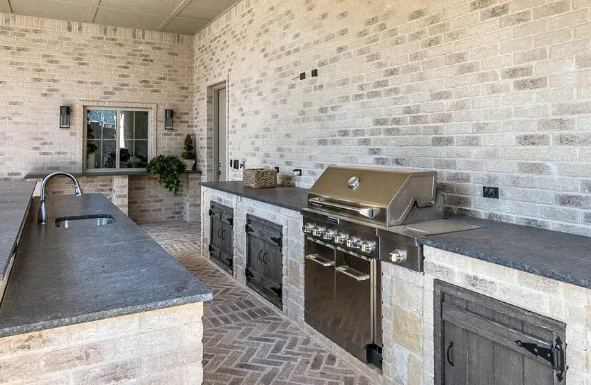 Outdoor kitchen with black granite countertops and herringbone brick floor