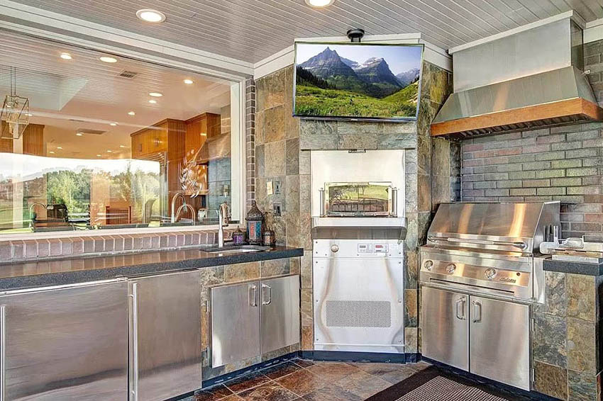 Outdoor kitchen with black laminate countertops, slate sides and brick backsplash