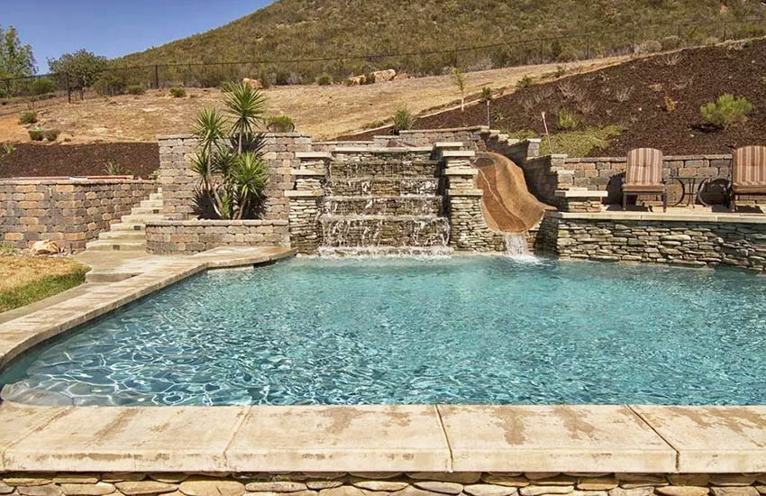 Swimming pool with stacked stone water feature retaining wall and patio