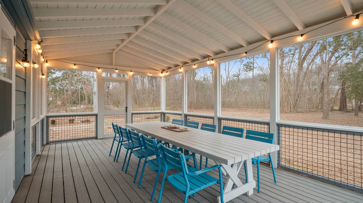 Open porch with Edison string lights, white farmhouse dining table, turquoise chairs, and wood deck