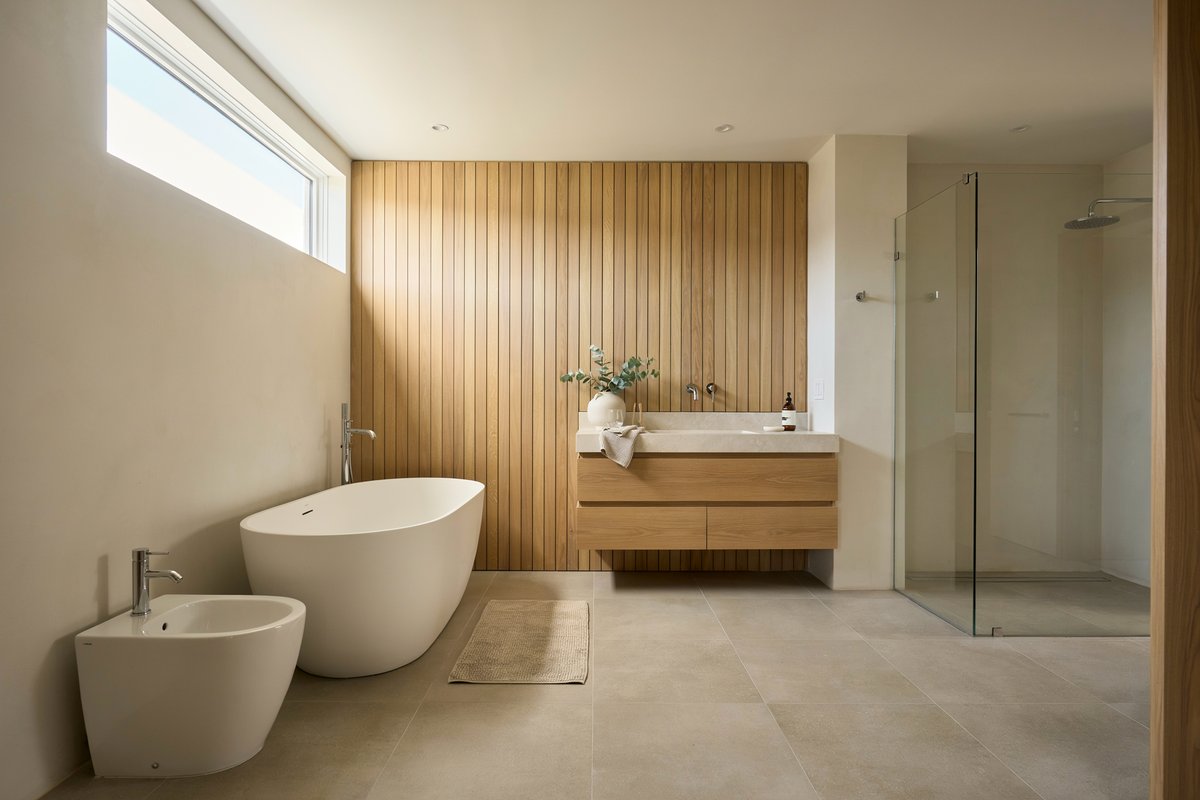 A wood-panel bathroom with white freestanding tub, floor bidet, and glass shower