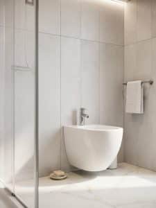 White ceramic standalone bidet against tiled wall beside a glass shower enclosure