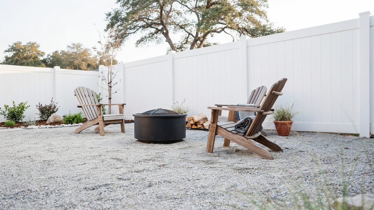 Crushed gray granite patio with black fire pit and white vinyl fence