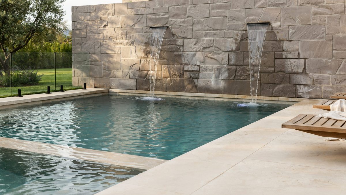 Rectangular pool with stone wall fountains spilling into clear blue water