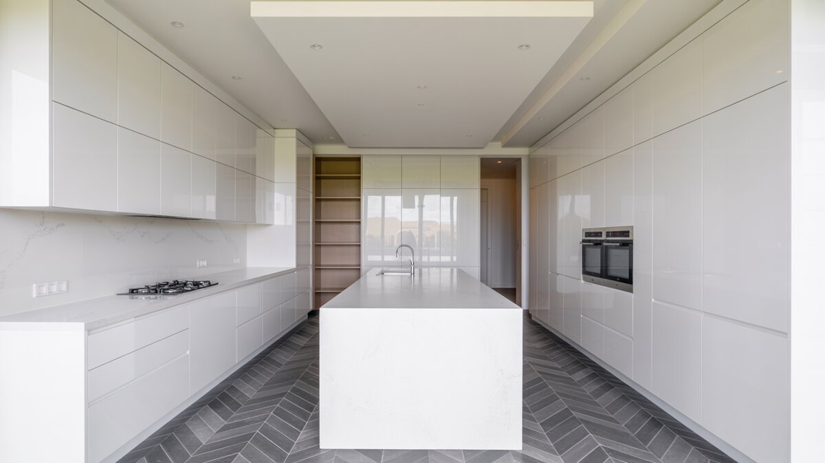 Ultra-minimal white gloss kitchen with long peninsula and gray herringbone tile floor