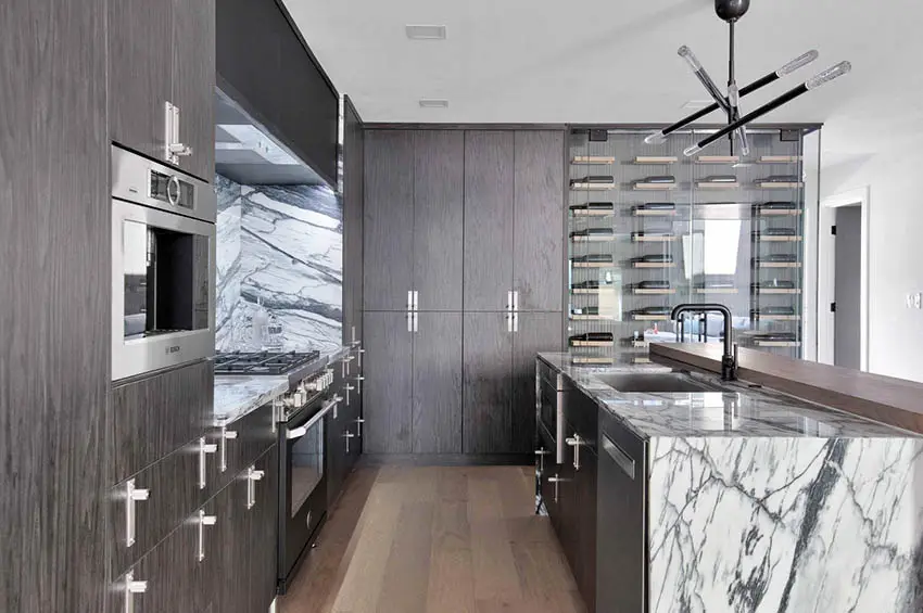Modern kitchen with dark cabinets wine closet and waterfall quartz island