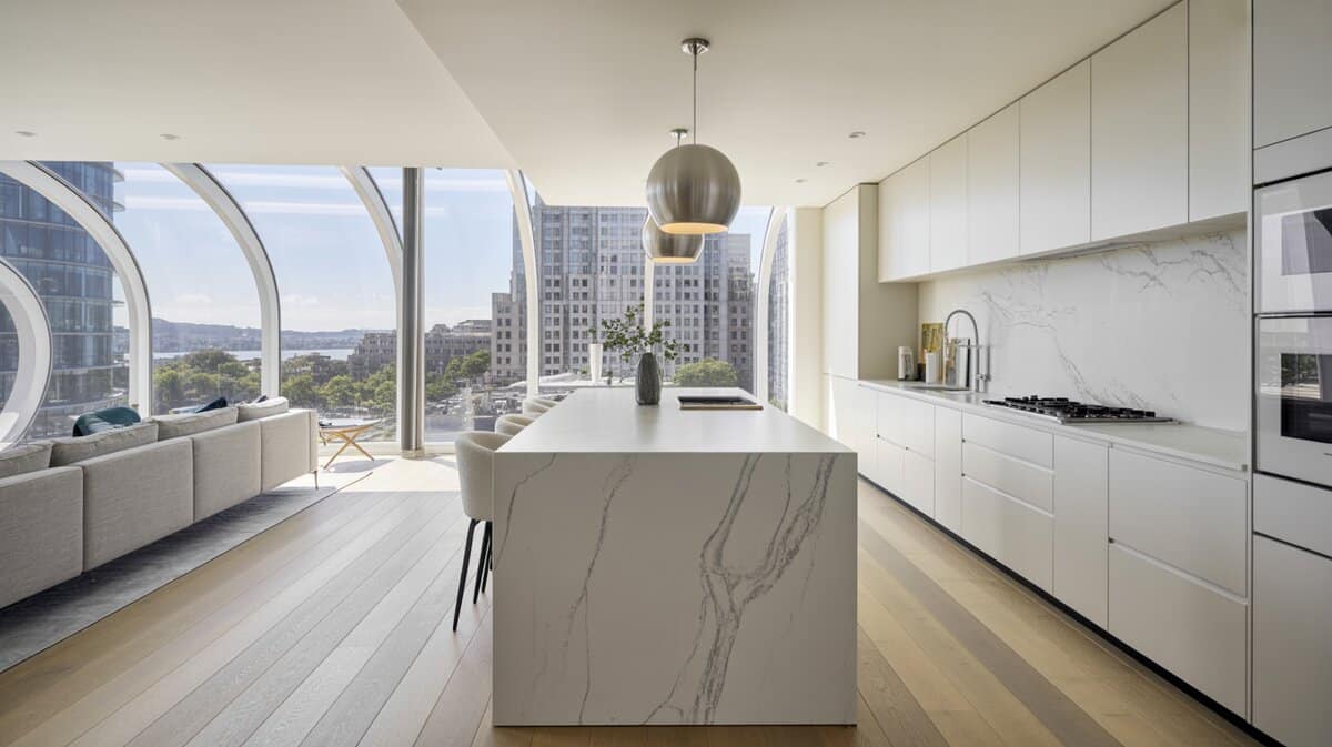 Ultra-modern white kitchen with marble waterfall island and curved floor-to-ceiling city views