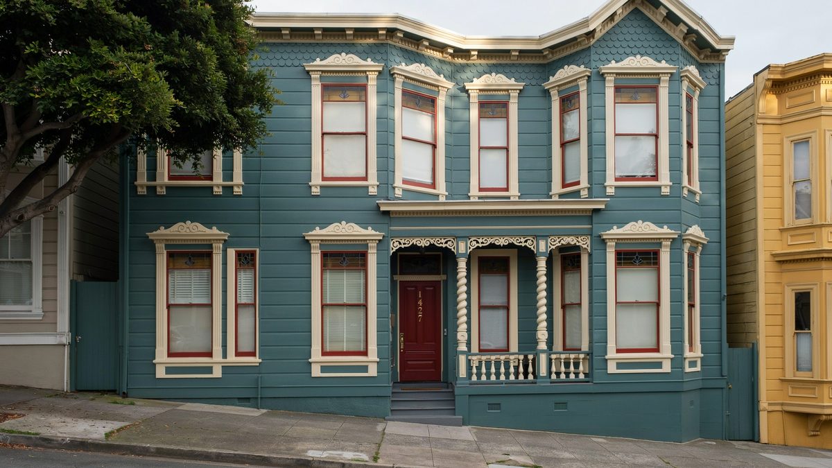 Slate blue Victorian with rope columns, red trim and a burgundy door beside a yellow neighbor
