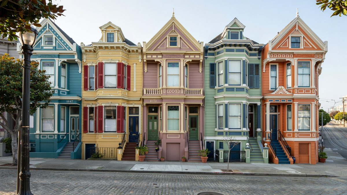 Five attached Victorians in teal, red, pink, mint and orange along a sloped street
