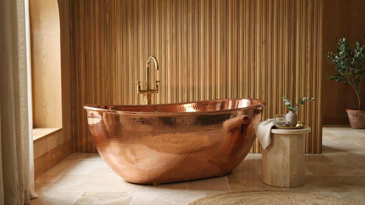 Hammered copper tub with dimpled sides against a warm wood slat wall