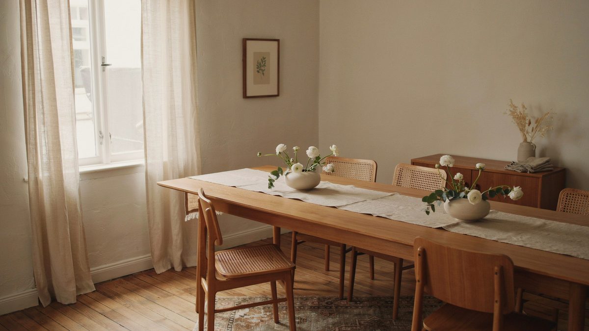 Long wood dining table with a linen runner and two white ranunculus bowls