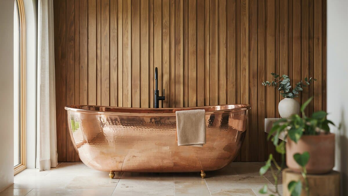 Freestanding copper tub in front of a vertical walnut slat accent wall