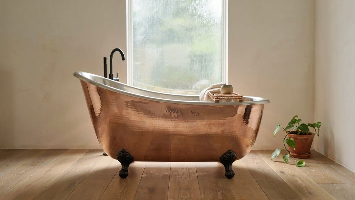 Copper slipper tub with one high raised end set near a garden window