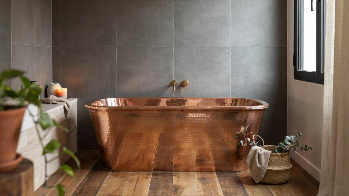 Compact deep hammered copper soaking tub against a large format grey tile wall