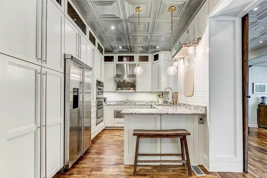 High ceiling kitchen with white cabinets tin ceiling tiles pendant lighting and granite peninsula