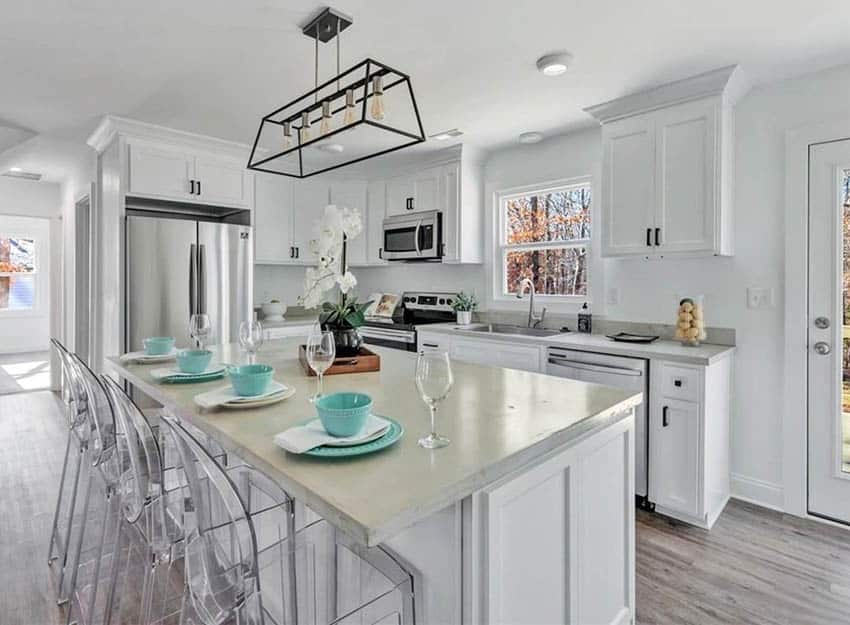 Kitchen with concrete countertops island and white cabinetry with black hardware