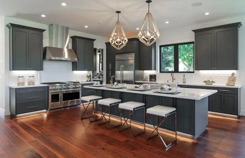 Kitchen with dark gray cabinets island white quartz counters and teak flooring
