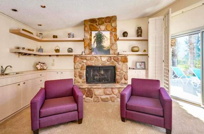 Room with stone fireplace, open shelves and pink accent chairs