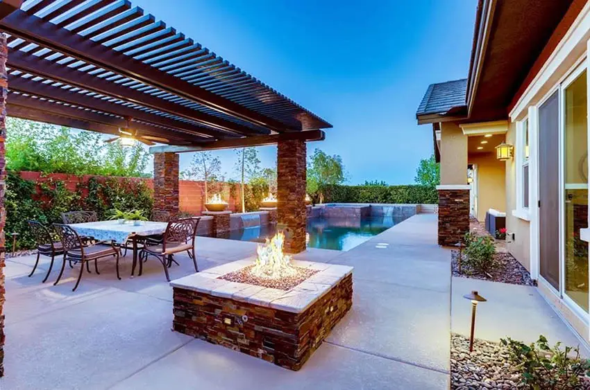 Modern metal pergola with stacked stone support posts=and fire pit