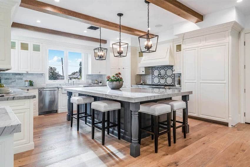 Open concept kitchen with marble countertop, gray island, white raised panel cabinets and wood beam ceiling