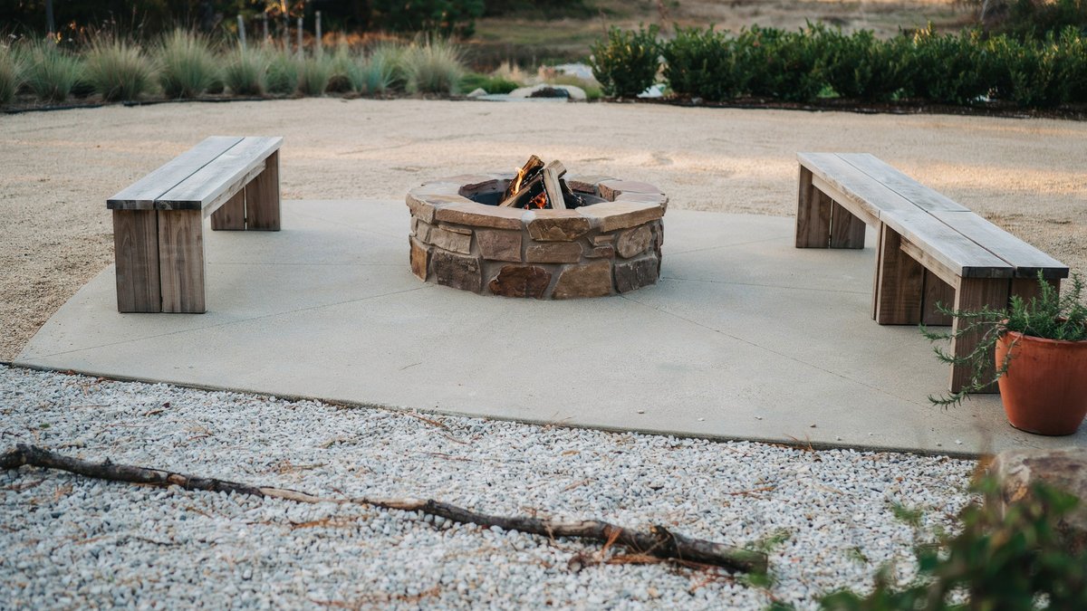 Two long wood benches facing a fieldstone fire pit on poured concrete
