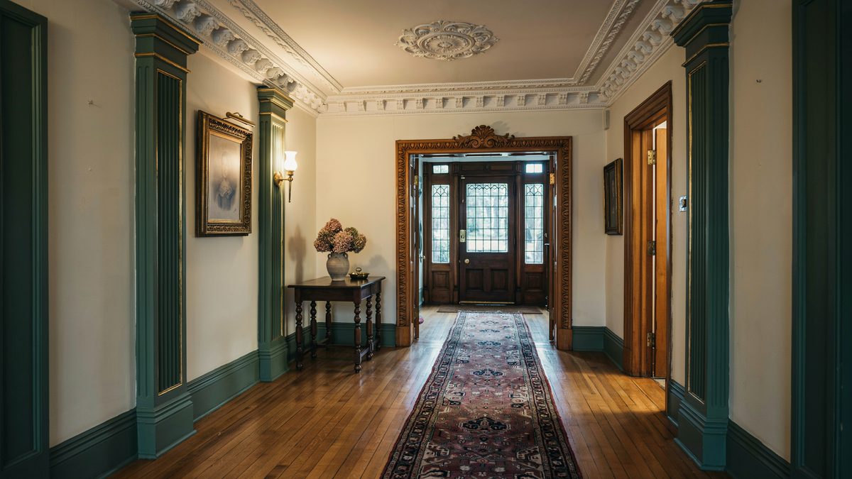Deep green entry hall with ornate ceiling medallion, paneled columns and a runner rug