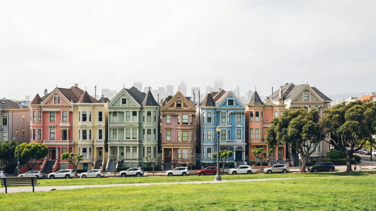 Painted Ladies row seen across Alamo Square lawn with fog over the downtown skyline