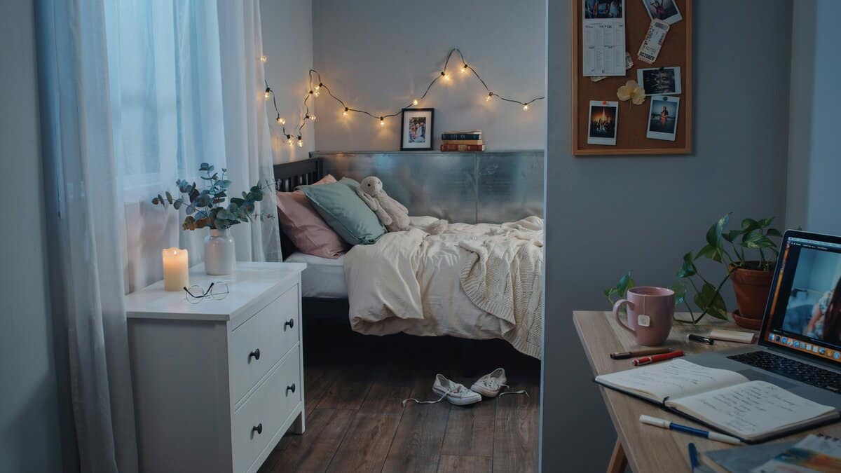 String lights draped above a bed beside a corkboard and small workspace