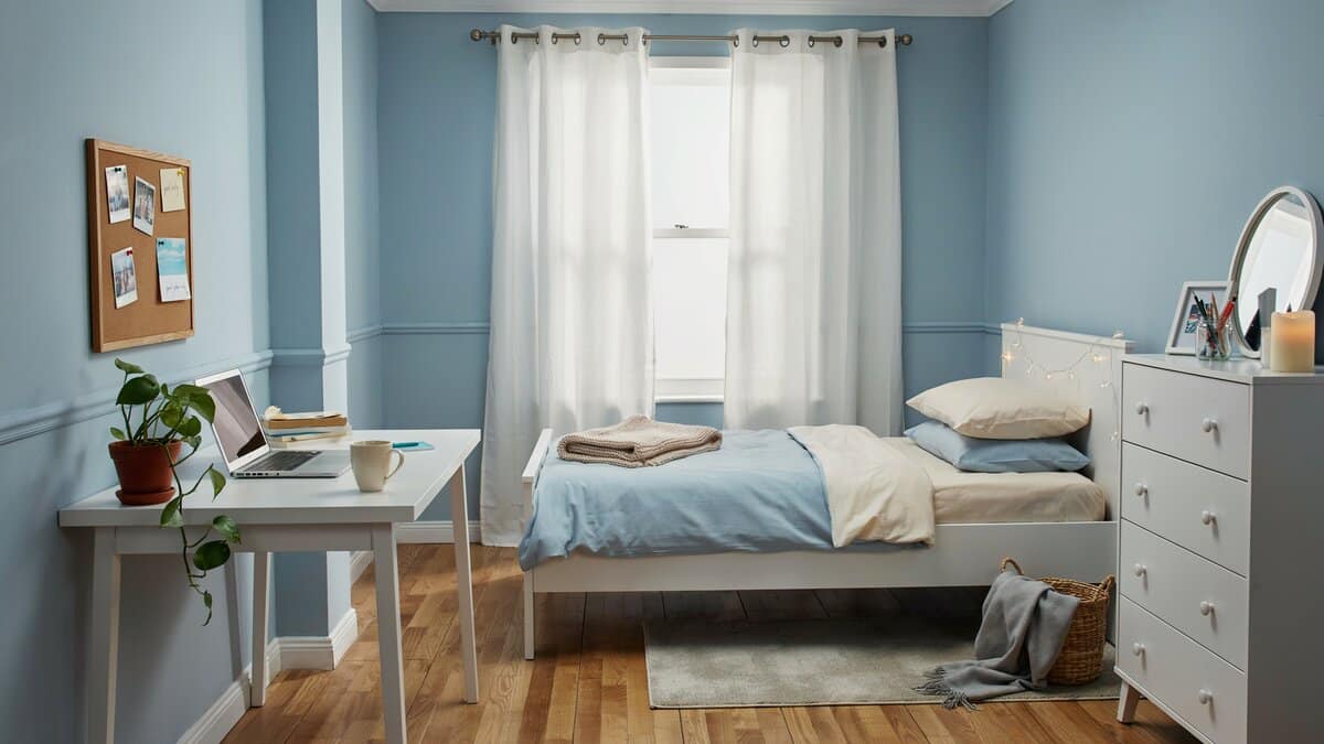 Pale blue bedroom walls with a white bed, dresser and small study desk