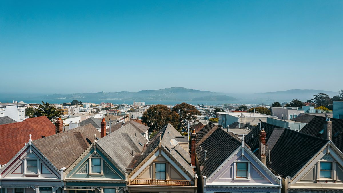 Gabled Victorian rooftops layered above the bay with distant hills and hazy blue sky