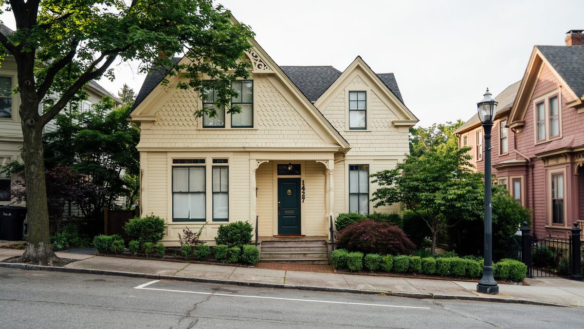 Pale yellow Victorian cottage with steep gable, clipped hedges and a black entry door