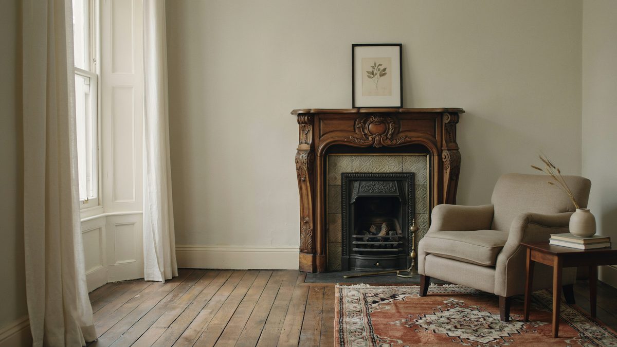 Carved walnut mantel over a tiled firebox beside a linen armchair on plank flooring