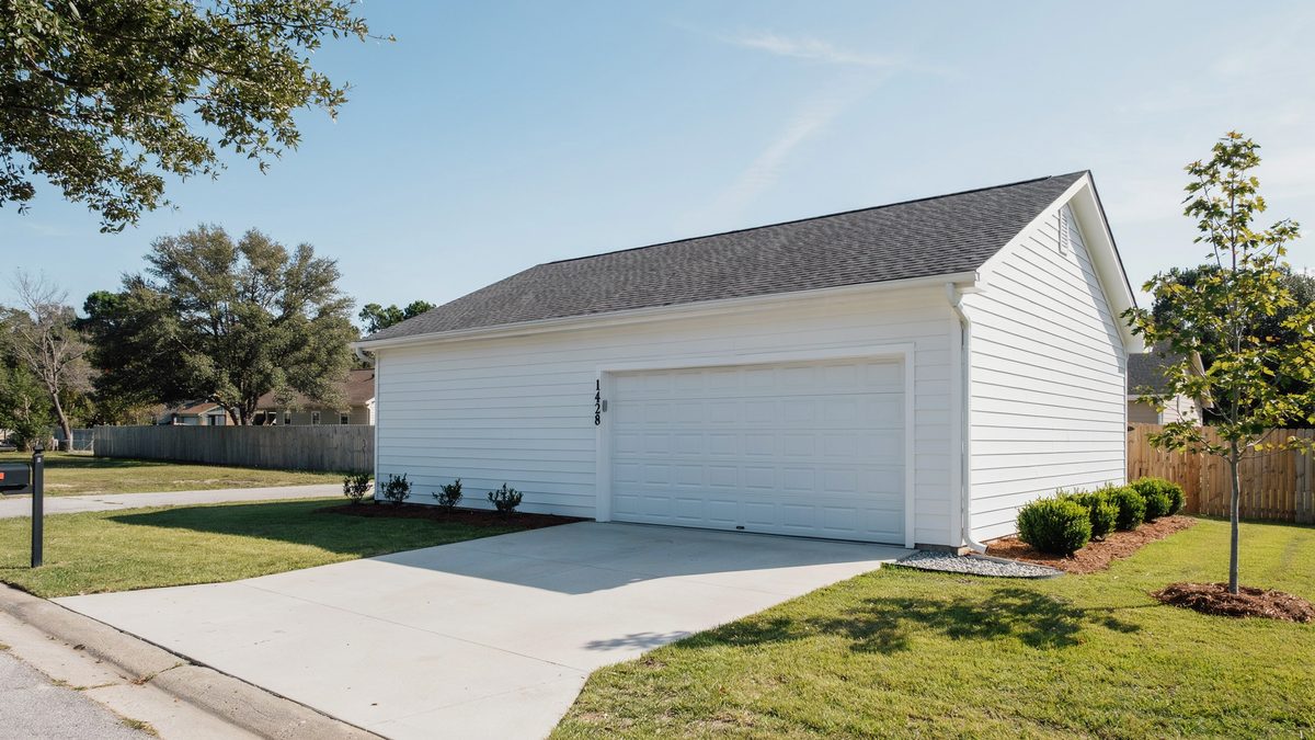 White single door detached garage with concrete driveway and trimmed green lawn