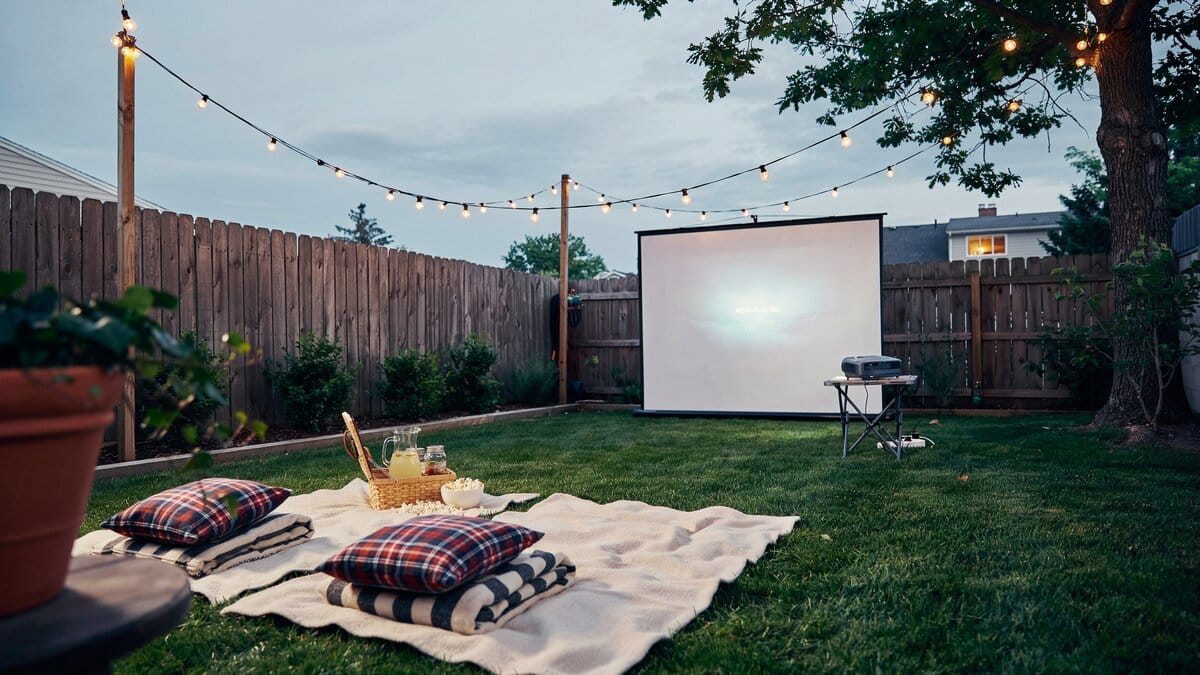 Backyard movie night with a projector screen blankets and string lights